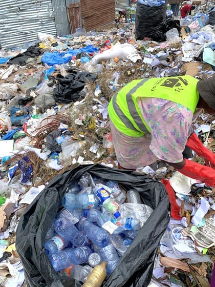 Travailleur en gilet haute visibilité triant à la main des bouteilles plastiques parmi les déchets collectés.